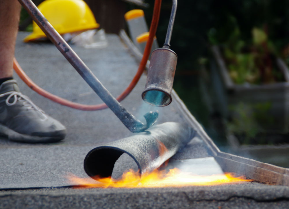 Roofer applying torch-on membrane to flat roof